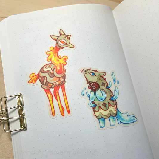 A photo of the two stickers stuck onto a page in a notebook, showing what they look like outside of the context of the sticker sheet.