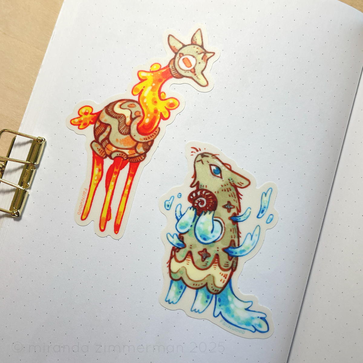 A photo of the two stickers stuck onto a page in a notebook, showing what they look like outside of the context of the sticker sheet.
