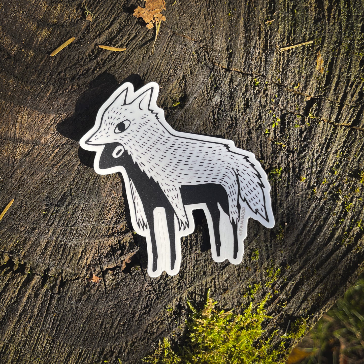 Matte vinyl sticker of a stylized and illustrated "sheep in wolves clothing". The sticker is photographed on a mossy stump.