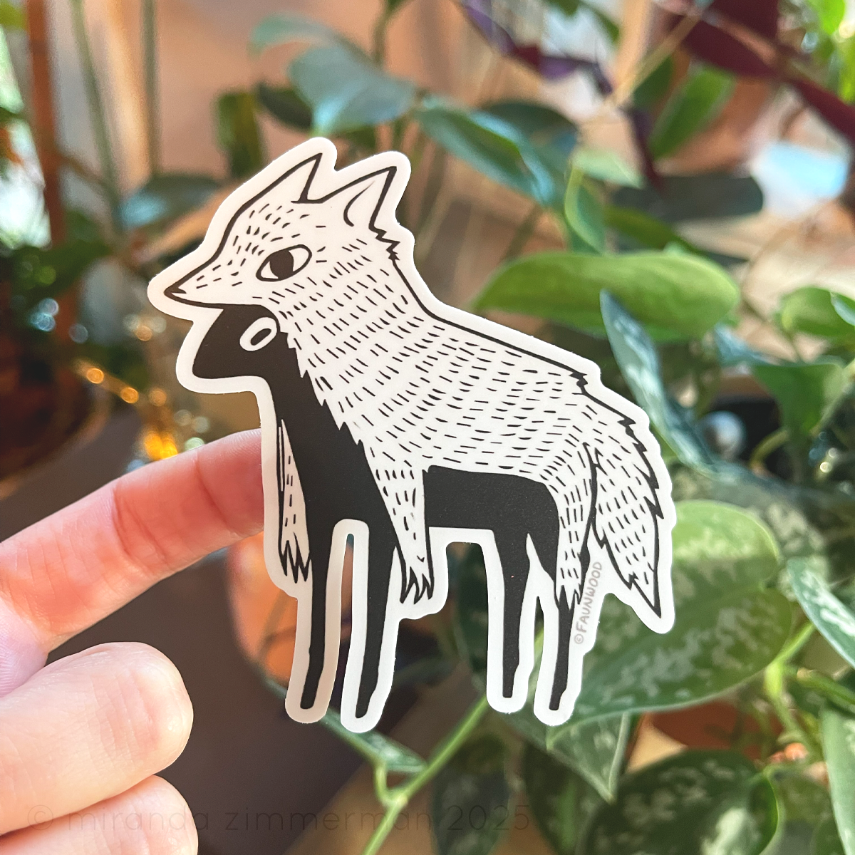 Hand holding a matte vinyl sticker of a stylized and illustrated "sheep in wolves clothing".  Photo is depicting the extra kiss cut areas between the legs.