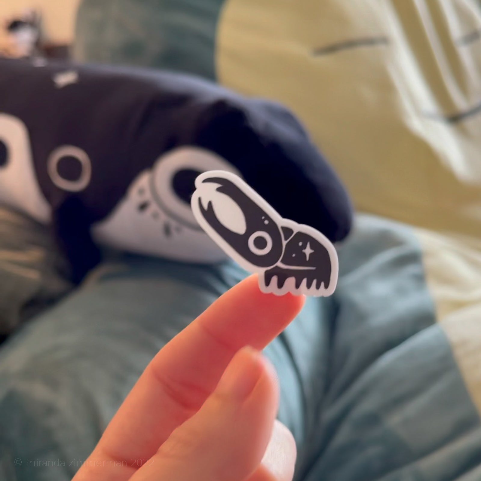 A small individual beetle sticker (removed from the sticker sheet) held by a hand against a blurry background.